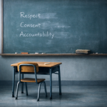 A child-sized desk and chair in an empty classroom. A chalkboard behind them shows partially erased words: “Respect,” “Consent,” and “Accountability.”